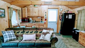 L’intérieur chaleureux d’un chalet avec une table à manger en bois, un canapé agrémenté de coussins à motifs d’élans, un coin cuisine doté de meubles en bois et une pancarte sur laquelle on peut lire « SIMPLIFIEZ ».