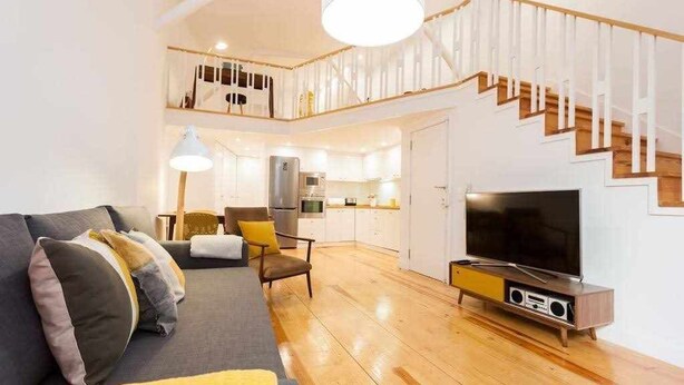 A modern living room with a sofa, TV, and wooden flooring.