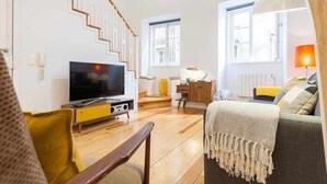 A living room with a staircase, a television, a desk, and a sofa.