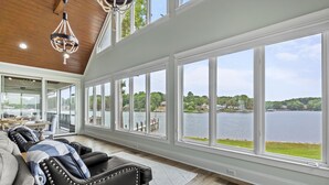 A spacious room with a large window overlooking a lake, a leather sofa, and a dining area.