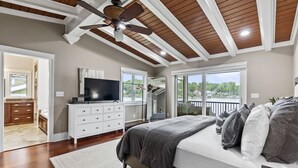A bedroom with a large bed, a ceiling fan, a TV, and a view of the outdoors.