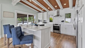 A modern kitchen with white cabinetry, a wooden ceiling, and a central island with bar stools.