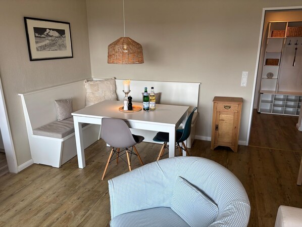 Un coin repas comprenant une table blanche, deux chaises, un banc, un luminaire suspendu et un petit meuble.