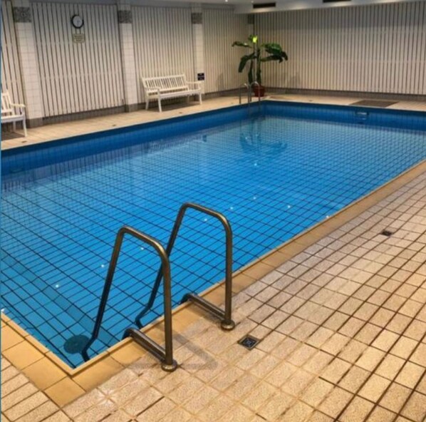 Ein Innenpool mit gefliestem Boden, einer Metallleiter und einer Sitzbank.