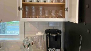 A kitchen with a coffee maker, a cabinet with cups and glasses, and a window with a view. - Bright & Cozy, Yarmouth Cape Top Beaches! (Yarmouth)
