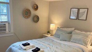A neatly made bed with a white and blue striped comforter, a bedside lamp, and decorative wall art. - Bright & Cozy, Yarmouth Cape Top Beaches! (Yarmouth)