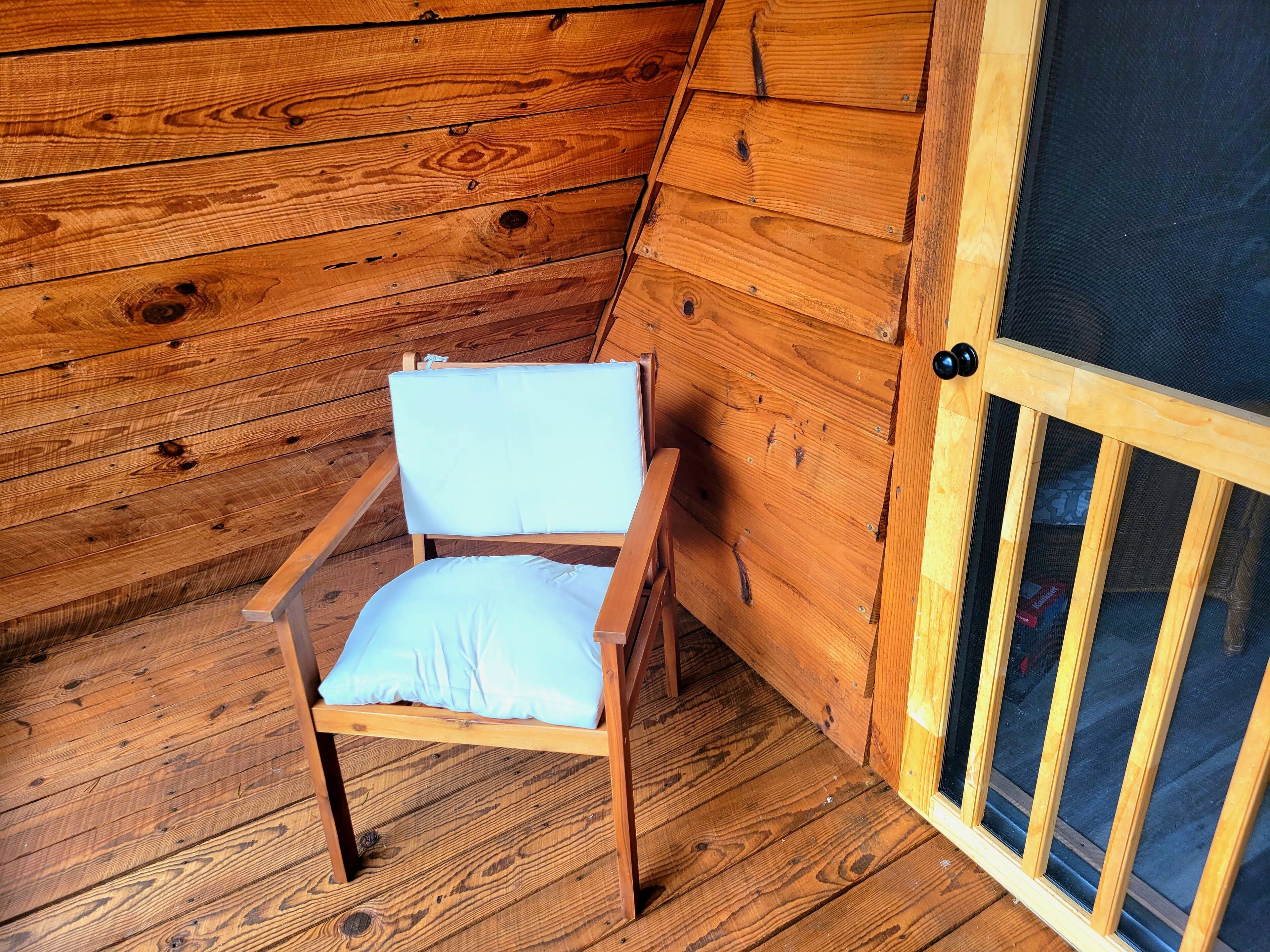 Una silla de madera con cojín en una habitación con paredes de madera y una puerta con mosquitera.
