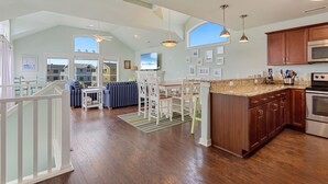 Una cocina amplia con armarios de madera, encimera de granito y una isla grande. Hay un comedor con mesa y sillas, y vistas a casas vecinas a través de ventanales.