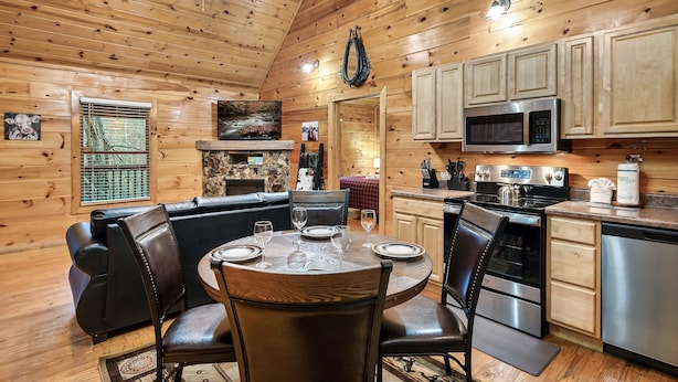 A cozy cabin-style kitchen with wooden walls, a dining area with leather chairs, and a built-in microwave. - Cozy Family Cabin, Hot Tub, Game Room, 2 King Beds Near Dollywood, Pet Friendly (Pigeon Forge)