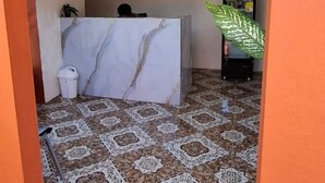 Zona de recepción con mostrador de mármol, suelo de baldosas estampadas, un cartel de bienvenida y una planta grande en maceta.