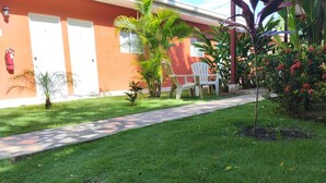 Pasillo de hotel con suelo de baldosas, plantas pequeñas y mobiliario exterior.