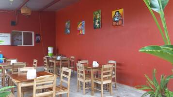A cafe with wooden tables and chairs, red walls, and various artworks.