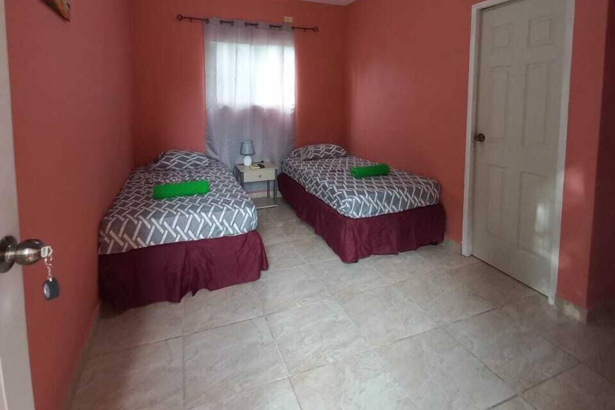 Quarto com duas camas, uma porta e uma janela com cortinas.