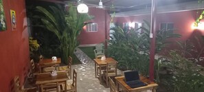Un comedor interior con mesas y sillas de madera, plantas en macetas y suelo de baldosas.