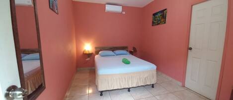 A bedroom with a bed, a nightstand, a wall-mounted air conditioner, a door, and a wall-mounted light fixture.