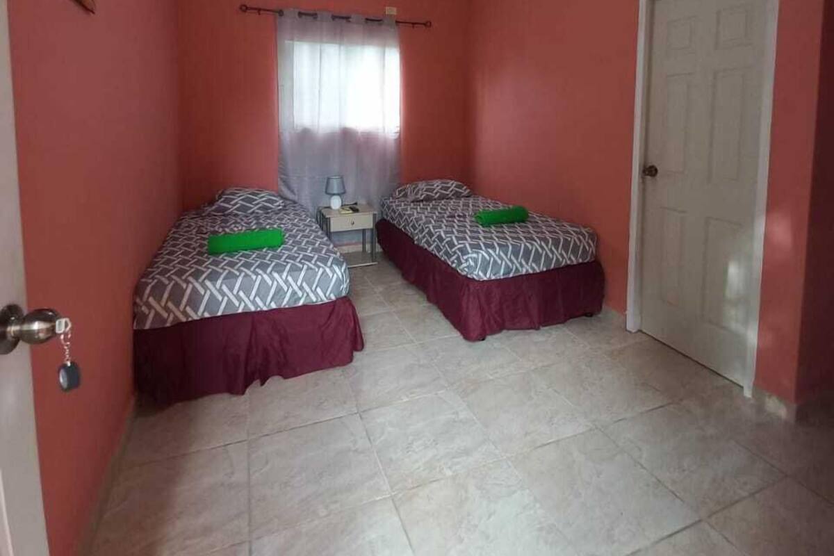 Quarto com duas camas, uma porta, uma janela com cortinas e uma luminária no teto.