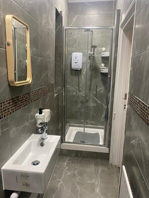 A modern bathroom with a glass-enclosed shower, a white sink with a soap dispenser, and a mirror with a gold frame.