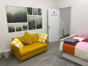 A room with a sofa, a bed, a door, and a wall with pictures.