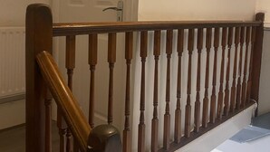 Escada com balaústres de madeira e corrimão, que leva a um quarto com porta branca e janela de vidro jateado.