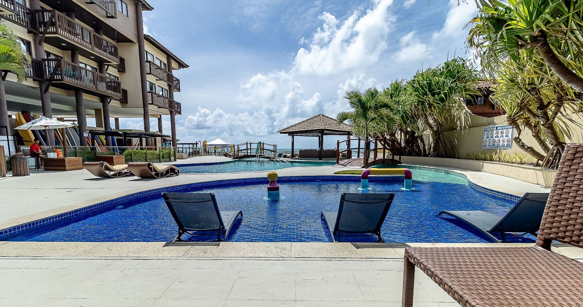 A swimming pool with lounge chairs, a lifeguard stand, and a building with balconies.