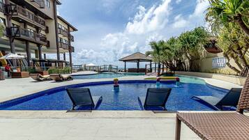 A swimming pool with lounge chairs, a lifeguard stand, and a building with balconies.