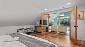 A bedroom with a bed, a bedside table, a dresser, a mirror, and a view of a balcony with a chair and a lamp. - kids secret room, Canoes/Kayaks, fire pit, ev charger. (Center Harbor)