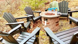 A stone fire pit surrounded by Adirondack chairs in a forest setting. - kids secret room, Canoes/Kayaks, fire pit, ev charger. (Center Harbor)