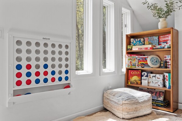 A room with a white wall, a pegboard with colorful balls, a bookshelf with board games, and a window with a view of trees. - kids secret room, Canoes/Kayaks, fire pit, ev charger. (Center Harbor)