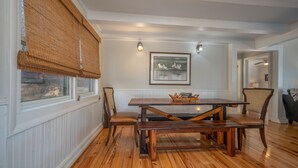 A dining area with a wooden table and chairs, a framed picture on the wall, and a window with a bamboo blind. - Cozy Tucked Away Log Cabin- Lake/Mountain views! (Lake Lure)
