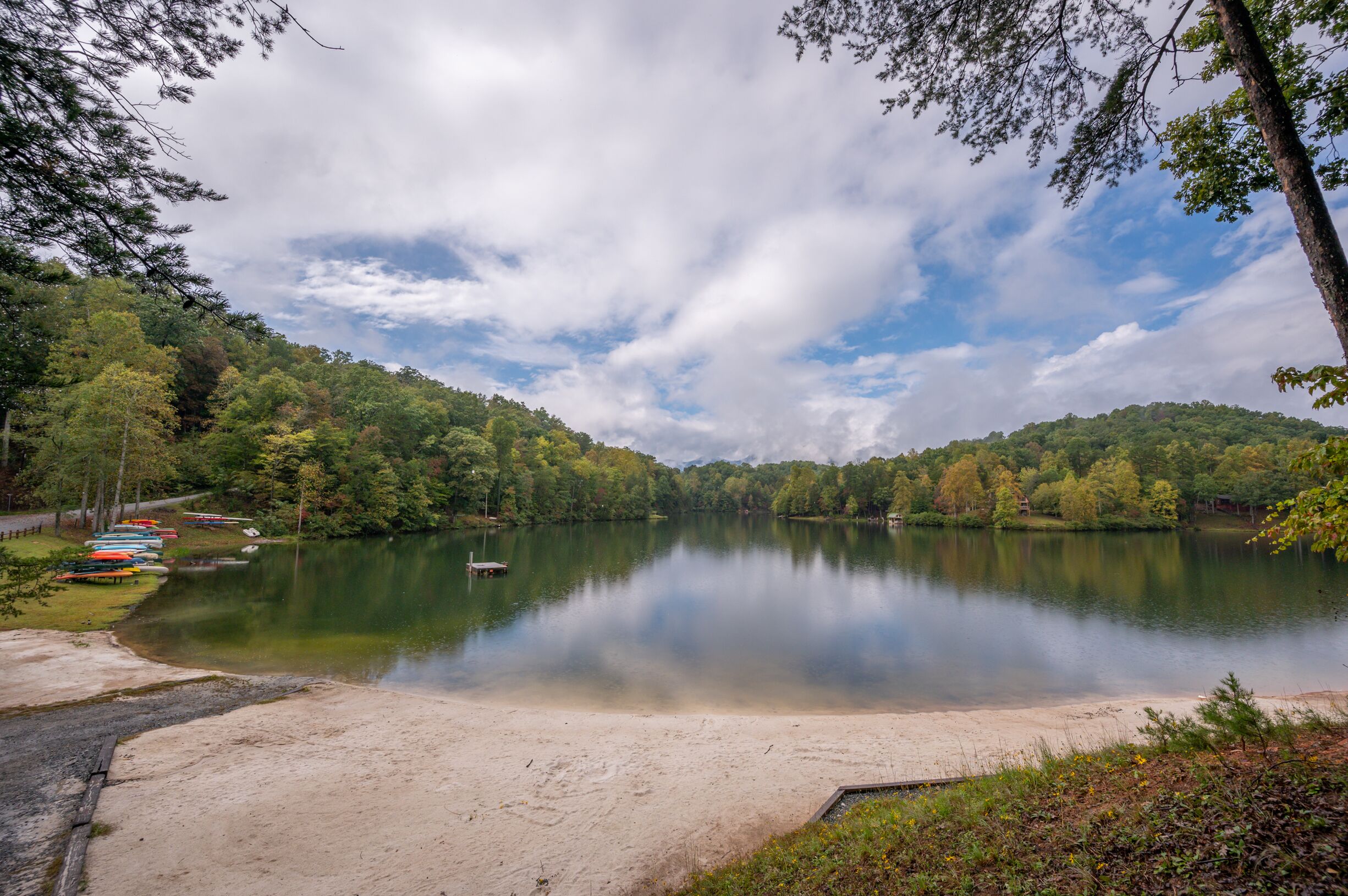 A calm lake surrounded by forested hills, a sandy beach, and several boats.
