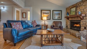 A living room with a stone fireplace, leather sofa, and a wooden coffee table. - Cozy Tucked Away Log Cabin- Lake/Mountain views! (Lake Lure)