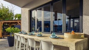 An outdoor bar area with a concrete countertop, white bar stools, and a woven basket. - Villa Cocolishi:Luxe Pool Retreat 5 Min->Beaches (Noord)