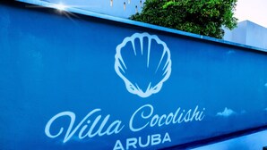 A sign for Villa Cocodishi in Aruba, featuring a shell logo and the name in cursive. - Villa Cocolishi:Luxe Pool Retreat 5 Min->Beaches (Noord)