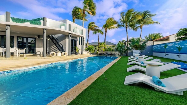 A modern pool area with a clear blue pool, white lounge chairs, and palm trees. - Villa Cocolishi:Luxe Pool Retreat 5 Min->Beaches (Noord)