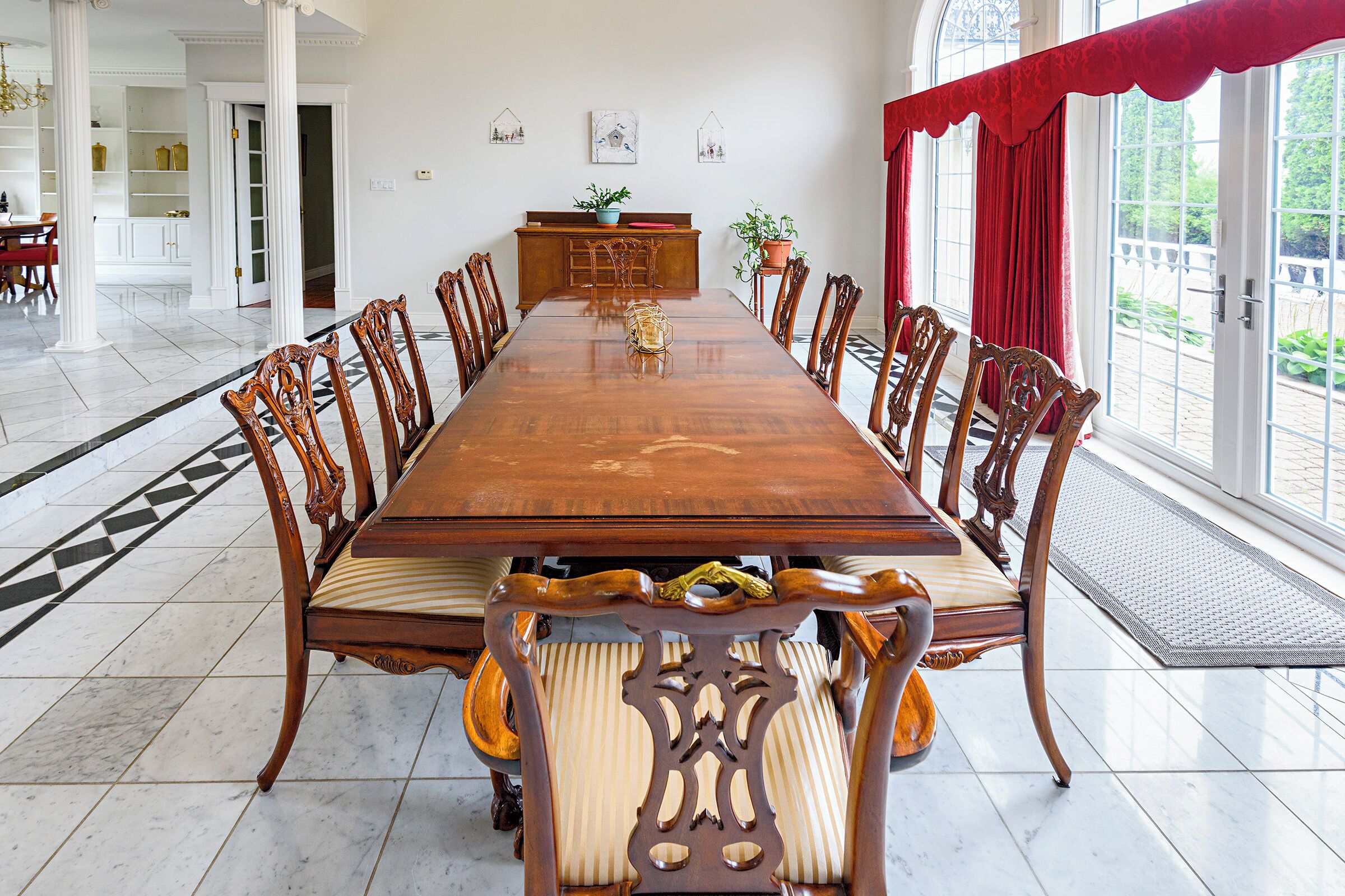 Une grande table à manger entourée de chaises élégantes, un buffet en bois et une vue sur l’extérieur grâce à de grandes fenêtres.