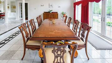 Une grande table à manger entourée de chaises élégantes, un buffet en bois et une vue sur l’extérieur grâce à de grandes fenêtres.