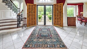 A grand entrance with a marble floor, a large ornate rug, and a view of a garden through open doors. - Mulgrave Vila (Mulgrave)
