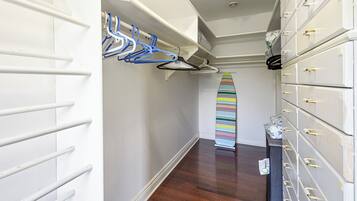 A hallway with a white wall, a wooden floor, a surfboard leaning against the wall, and a set of white storage drawers with gold handles.