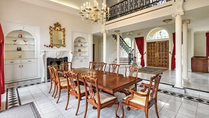 A spacious dining room with a large wooden table and ornate chairs, a grand staircase, and a fireplace. - Mulgrave Vila (Mulgrave)