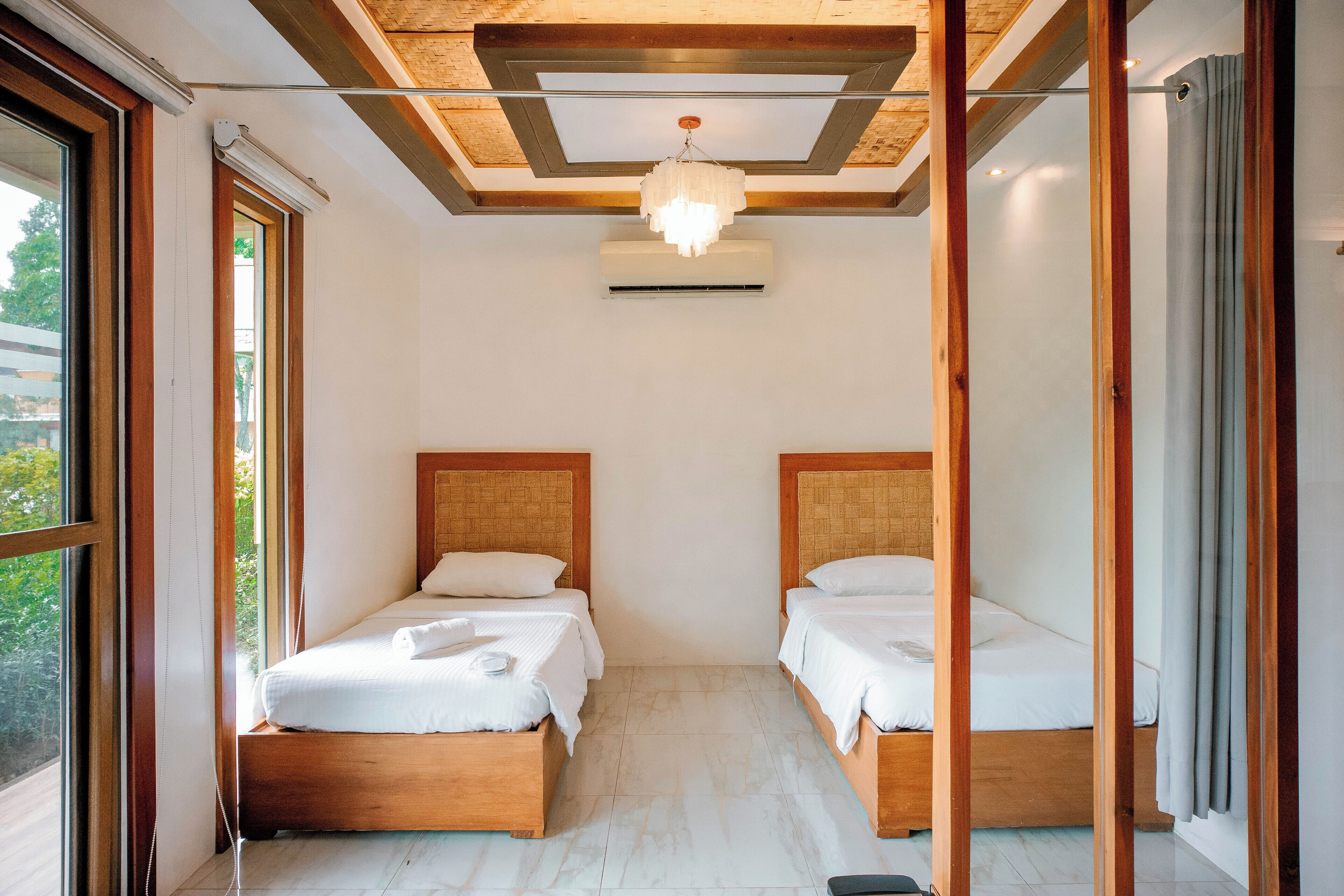 A room with two wooden beds, a ceiling fan, and a large window.