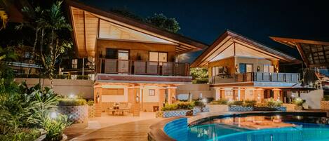 Un resort moderno con piscina, terraza de madera y varios niveles de espacios exteriores.