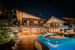 Un resort moderno con piscina, terraza de madera y varios niveles de espacios exteriores.