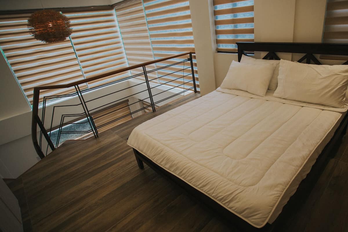 A bedroom with a bed, wooden flooring, and a view of the outdoors through large windows.