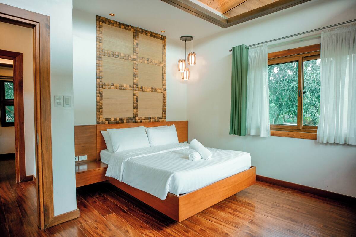 A modern bedroom with a wooden bed, a large window with curtains, and a unique wall design.