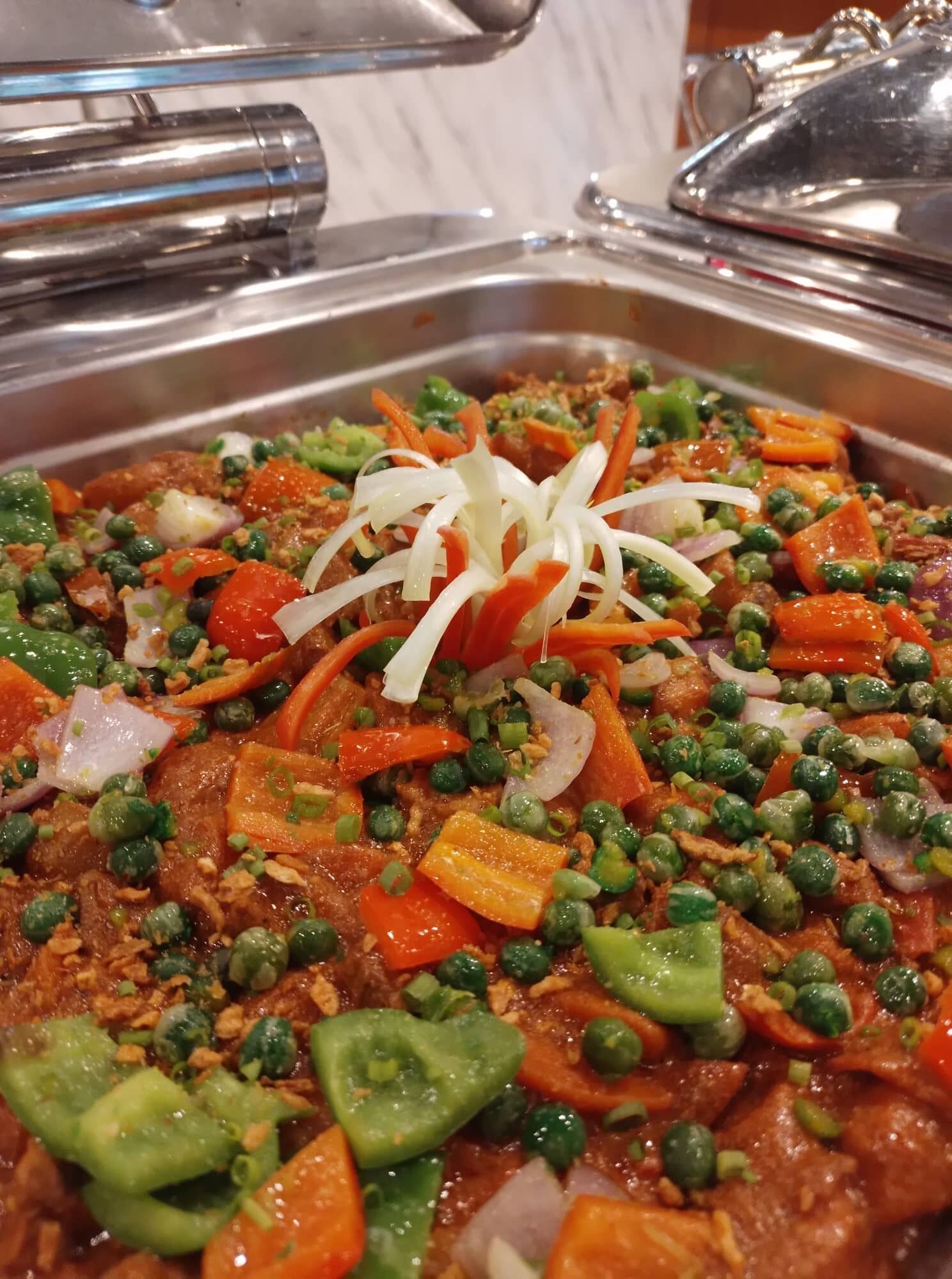 A buffet with a variety of dishes including meat, vegetables, and garnishes.