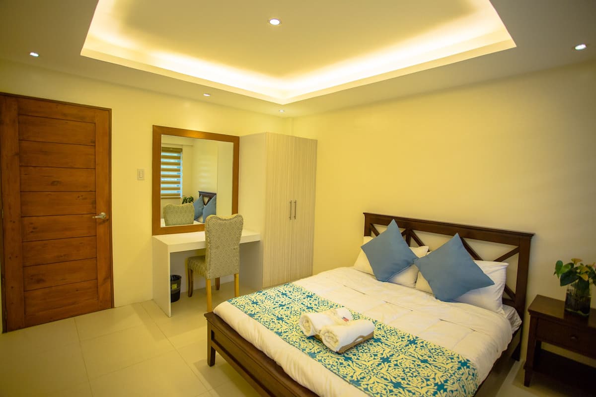 A bedroom with a bed, a desk, a chair, a wardrobe, and a mirror.
