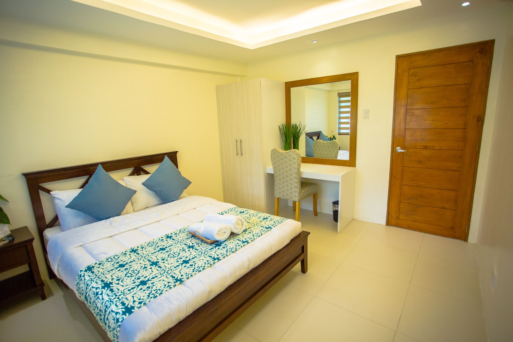 A bedroom with a bed, bedside table, chair, desk, mirror, and wardrobe.