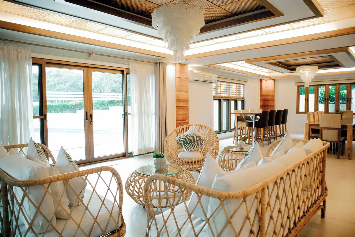 A spacious room with wicker furniture, large windows, and a chandelier.