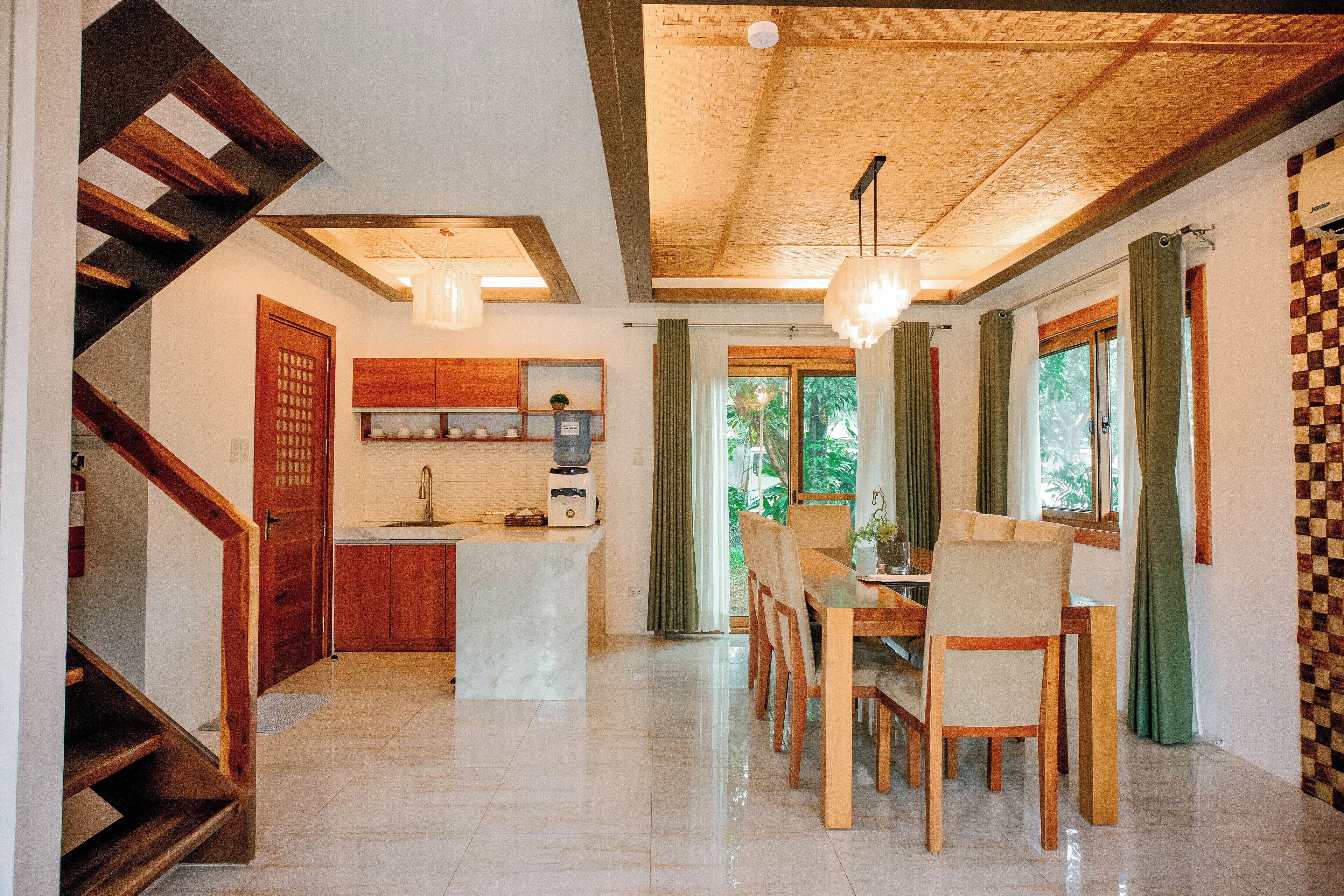 A modern kitchen with a marble countertop, wooden cabinets, and a built-in oven. There is a dining area with a wooden table and chairs, and a staircase with wooden railings.