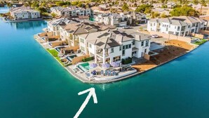 An aerial view of a residential area with houses along a waterfront, featuring a prominent house with a balcony and a flag. - 4 Private EnSuites, 270* Lake View, pool+spa, Sleeps 12 (Indio)